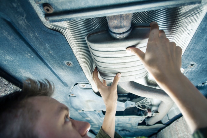 Male mechanic replacing exhaust pipe under car