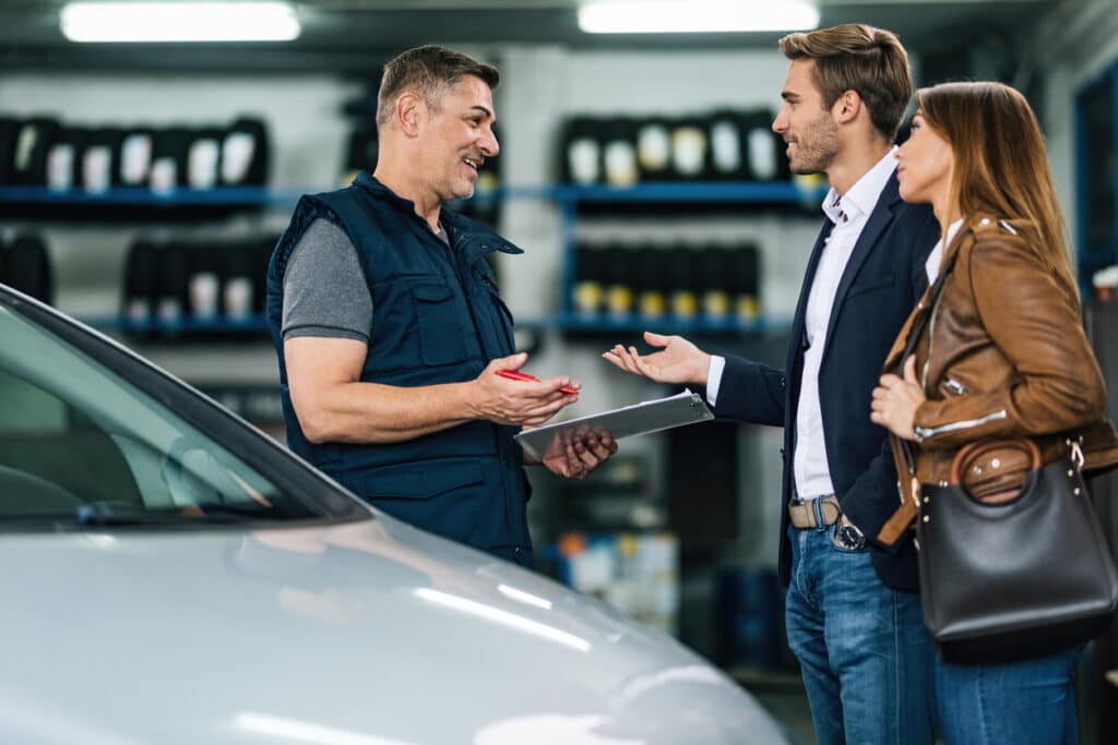 Happy auto repairman communicating with young couple in a workshop.