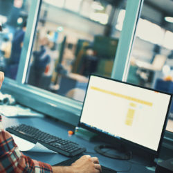 Closeup side view of a control room at a modern industrial production line with a control person in charge keeping track of the process on a computer.