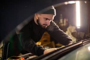 Young man servicing his car on his own at home in his garage. Shot from the front