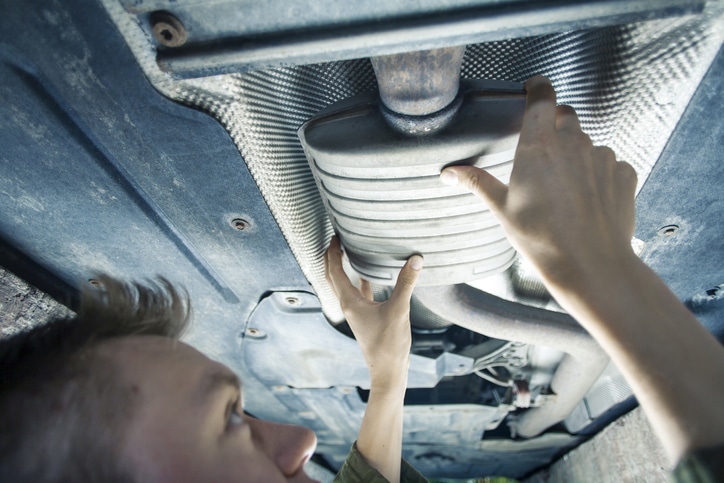 Male mechanic replacing exhaust pipe under car