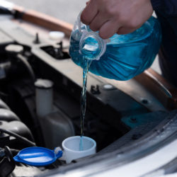 Man is holding bottle of blue antifreeze in hands and pouring antifreeze liquid for washing car screen
