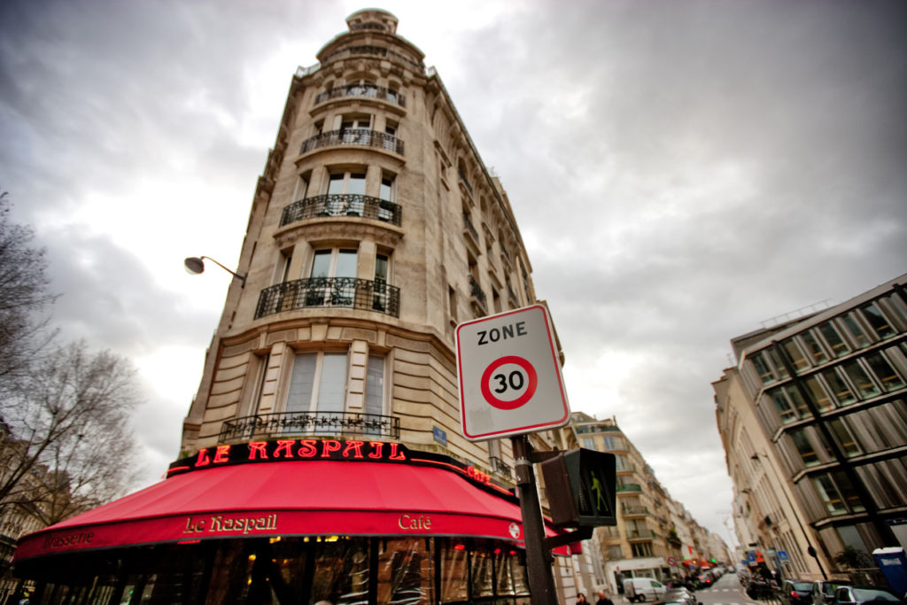 "Paris, France - December 26, 2012: Overcast Winter day in Paris, Le Raspail Cafe entrance, few people walking on the street, numerous cars parked."