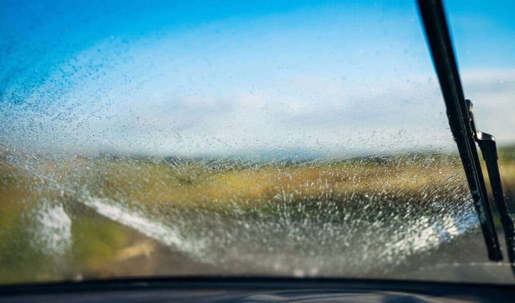 Water and cleaning fluid spraying onto a car's windscreen as a windscreen wiper clears the glass.