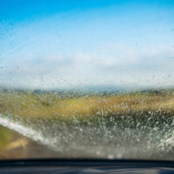 Water and cleaning fluid spraying onto a car's windscreen as a windscreen wiper clears the glass.