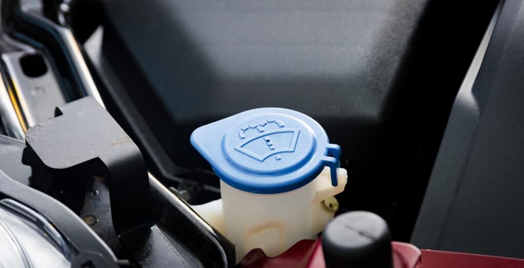 car windshield wiper cleaning spray water reservoir blue bottle cap with clear and communicative pictogram sign symbol show the liquid function inside, installed front under the hood near automobile engine