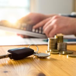 Car keys and money on table with man using calculator. Buyer counting savings and gas cost or salesman calculating sales price, vehicle value or road taxes.
