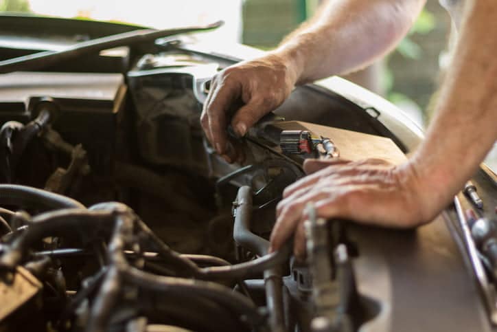 Auto mechanic working under the hood of an old car engine.