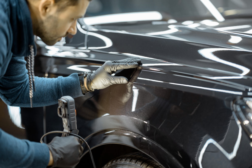 Car service worker examining vehicle body for scratches and damages, taking a car for professional auto detailing. Professional body car inspection concept