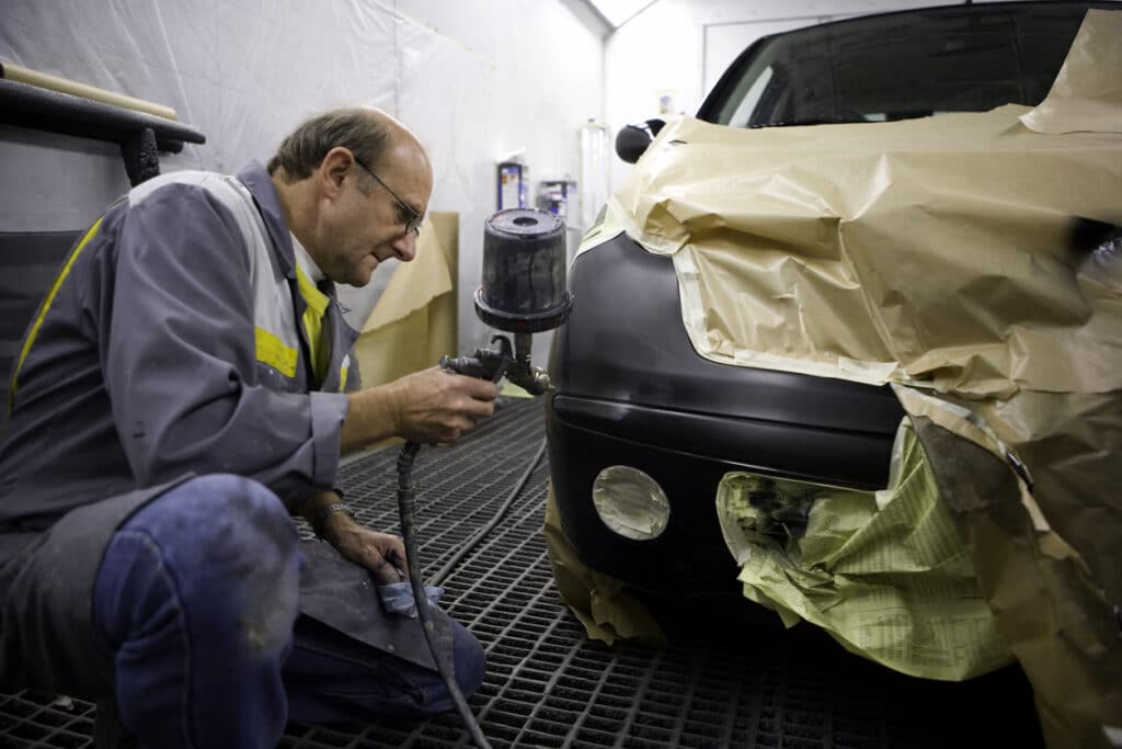 A mechanic is spraying a car portion in a special garage room.