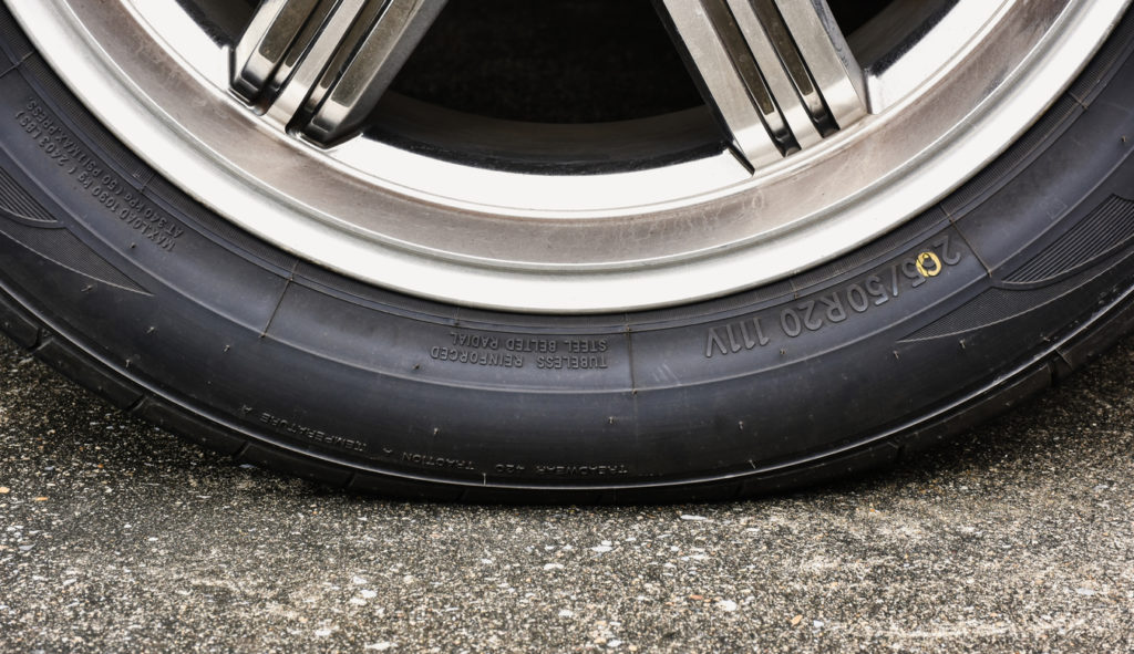 Sidewall of the car tire with a low tire pressure on the road,close up