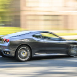 Ferrari F430 Italian sports car driving at high speed on a road through a forest near Baarn in Utrecht, The Netherlands during a sunny summer day.