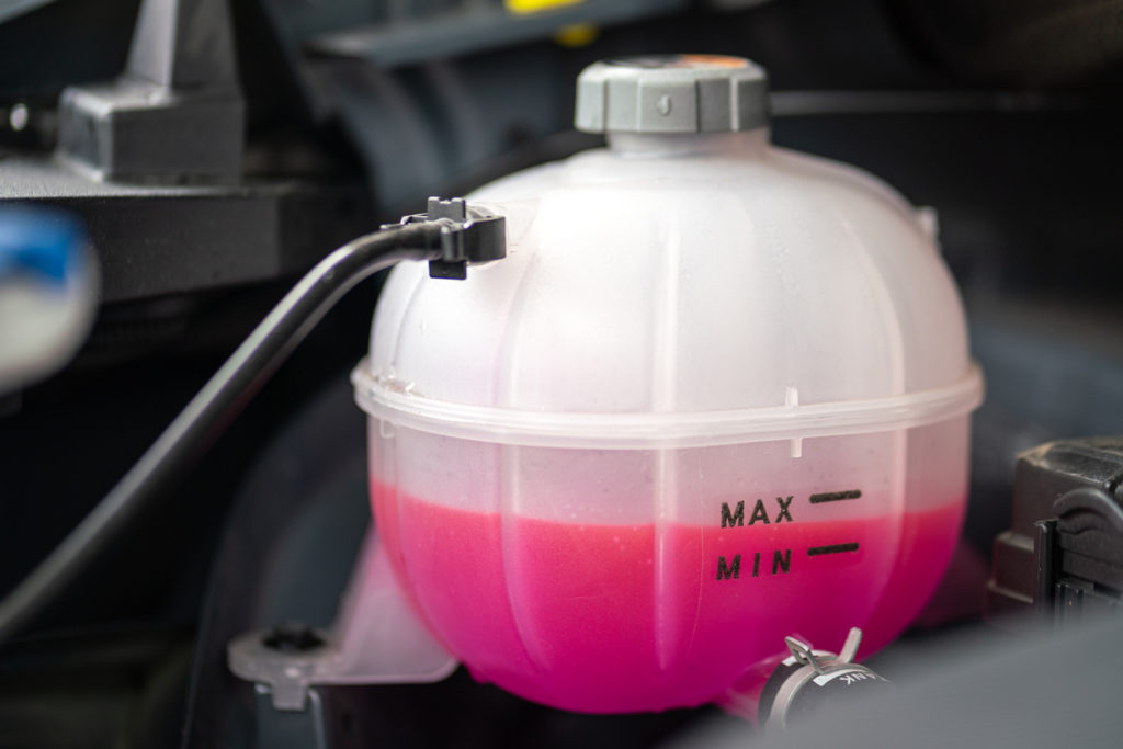 A car's engine coolant water supply box filled with pink color antifreeze liquid. Transportation equipment object photo.