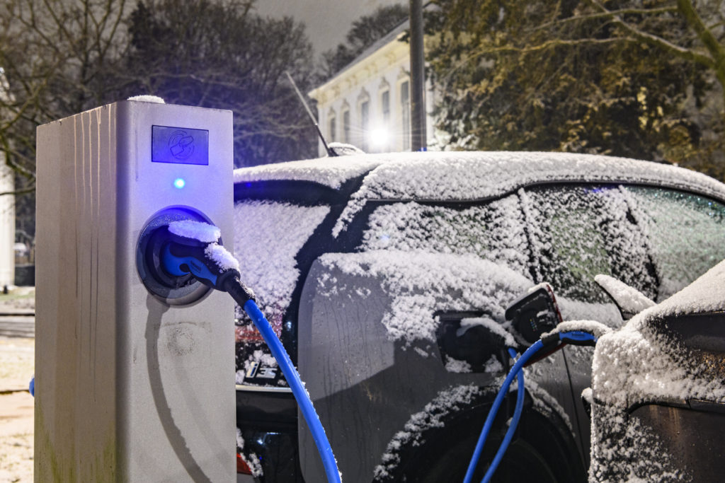 Electric cars charging at an electric vehicle charging station during a cold winter night in the city center of Zwolle. The BMW i3 and Tesla model 3 are covered in a thin layer of snow.