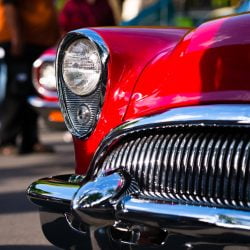 Retro Vintage red car with chrome accents headlamp grille and bumper reminiscent of the outline face predatory sharks in traditional outdoor exhibition of old cars in a small American provincial town.