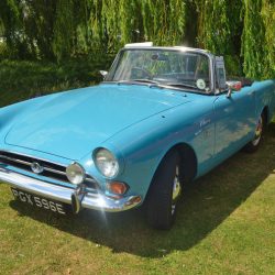 Classic Light Blue Sunbeam Alpine 2 door convertible motorcar restored and on show outside under willow trees.