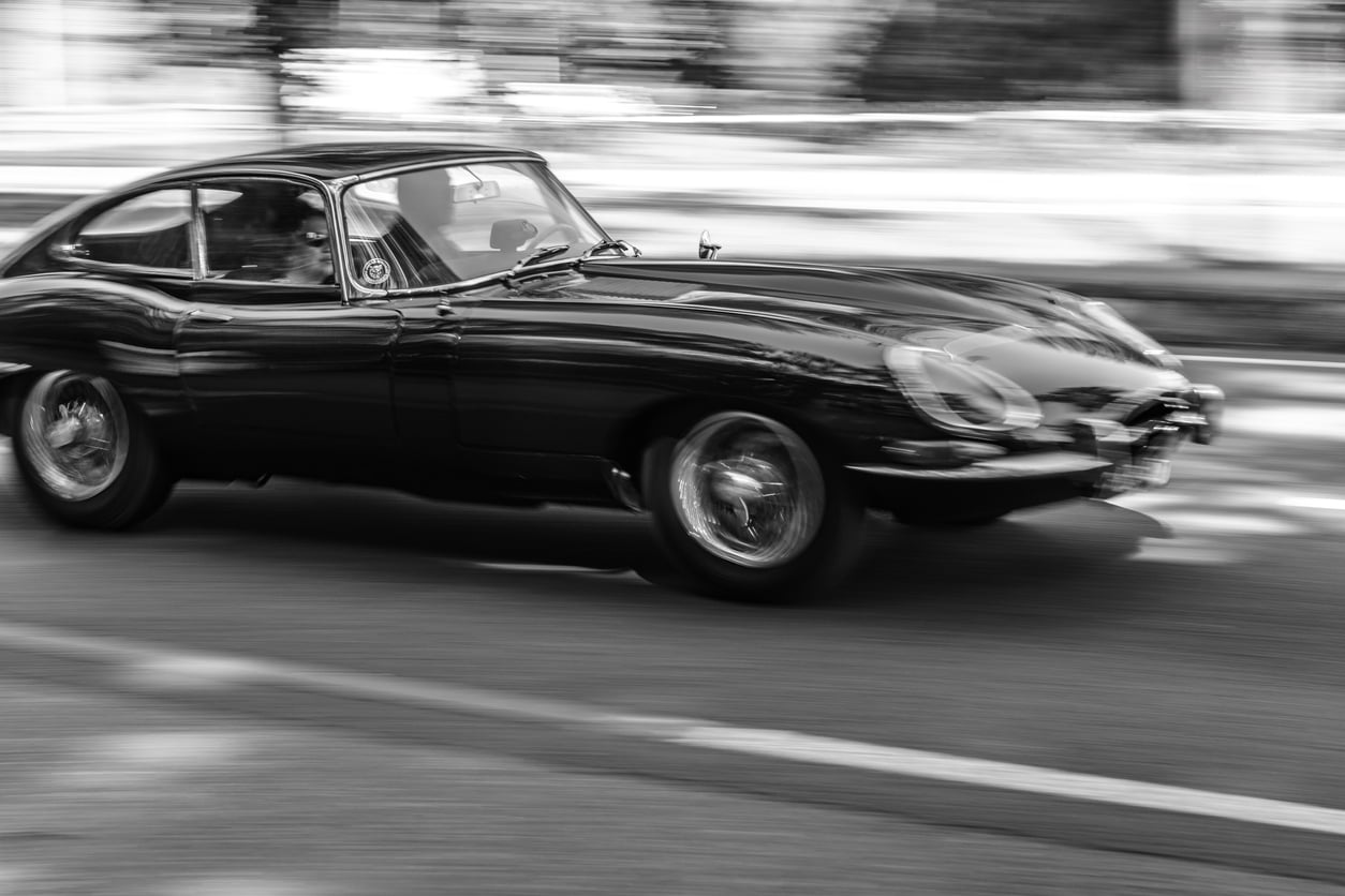 Jaguar E-Type driving at high speed on a road through a forest