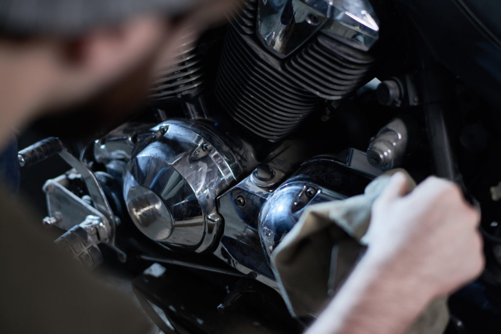 Close-up of mechanic examining motorcycle engine and wiping it in workshop