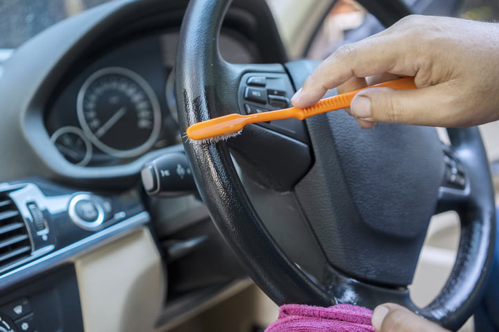 Worker hand using a brush to clean and remove dust or dirt on the steering wheel in a luxury car