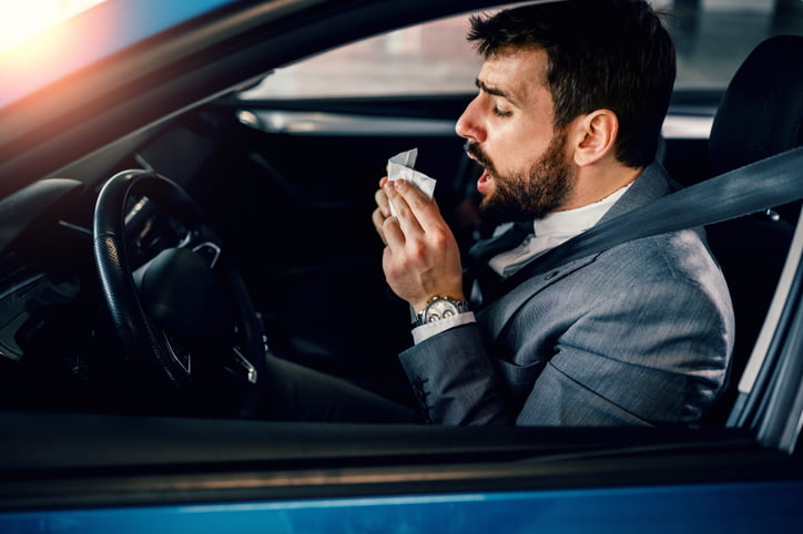 Businessman blowing his nose inside the car