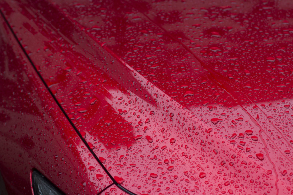 The surface of the car in raindrops. The red car is covered with water from precipitation.