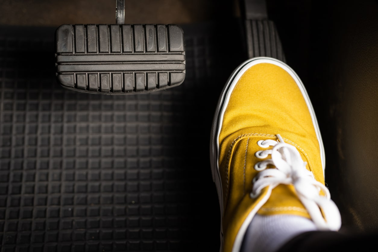 A man in yellow sneakers is stepping on the accelerator of a car