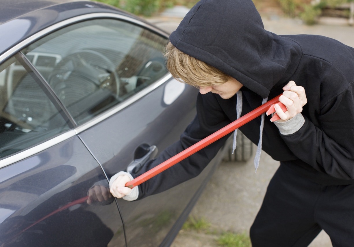 Burglar prying car window open with crowbar